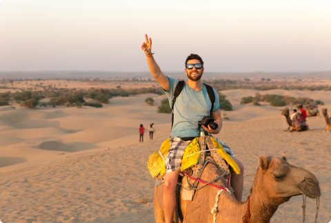 Man riding a camel in a desert giving the peace sign