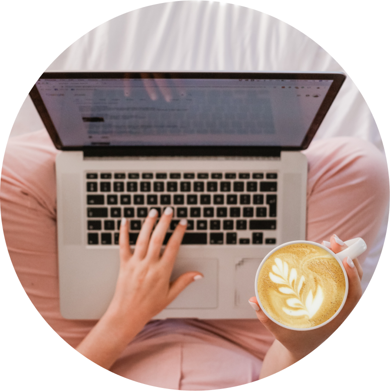 Someone typing on laptop in lap while holding a coffee