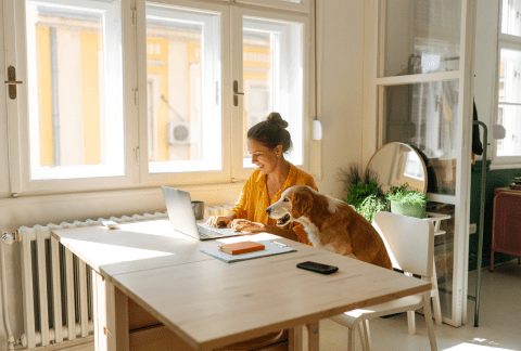 Woman and her dog at kitchen table looking at laptop